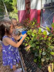 Children watering plants outside the classroom garden using spray bottles.