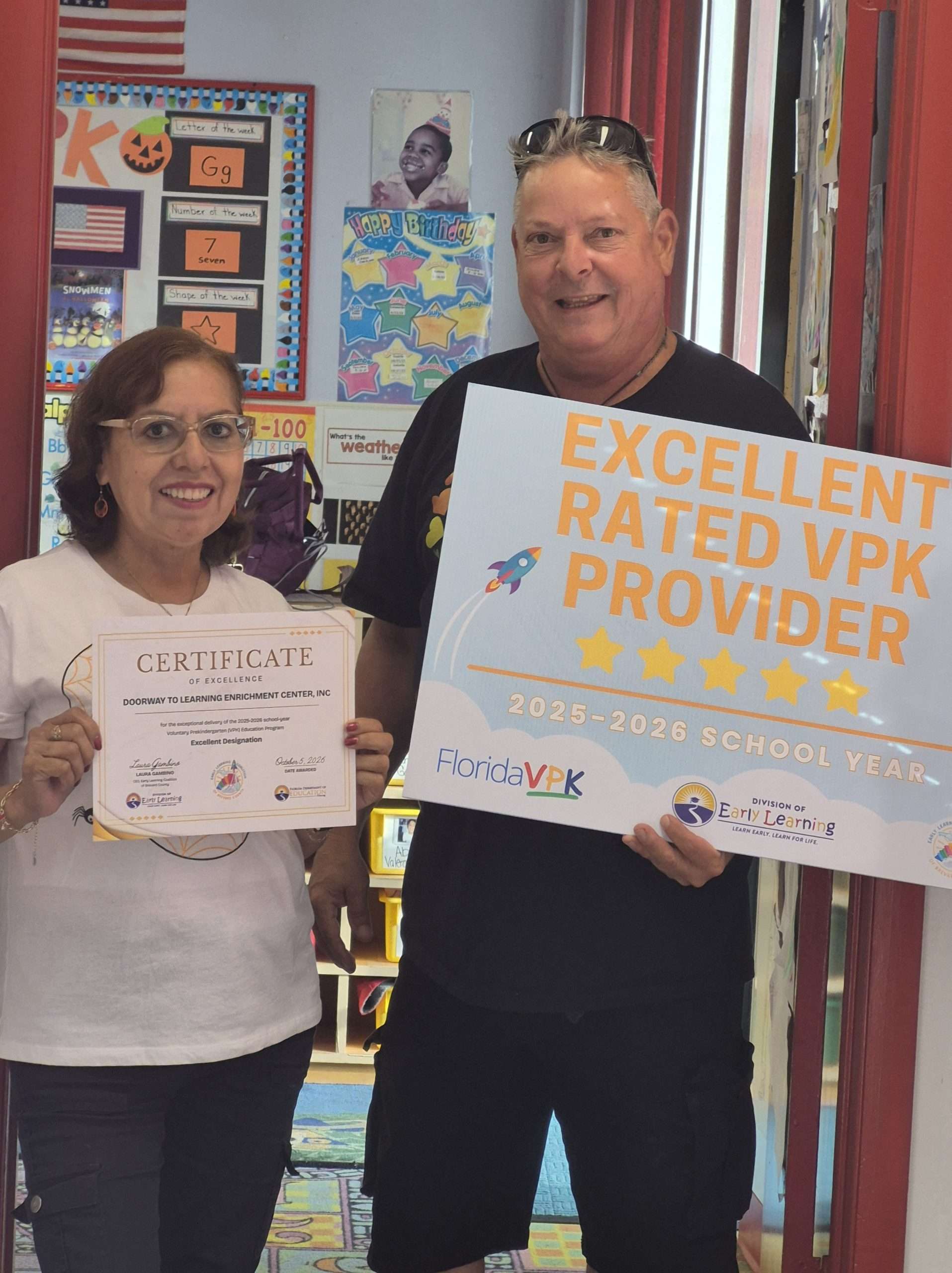Two people proudly displaying Doorway to Learning’s Excellent Rated VPK Provider recognition sign and certificate for the 2025–2026 school year.